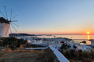 Sonnenuntergang auf Mykonos mit einem Windrad im Vordergrund und Blick über die Stadt Mykonos