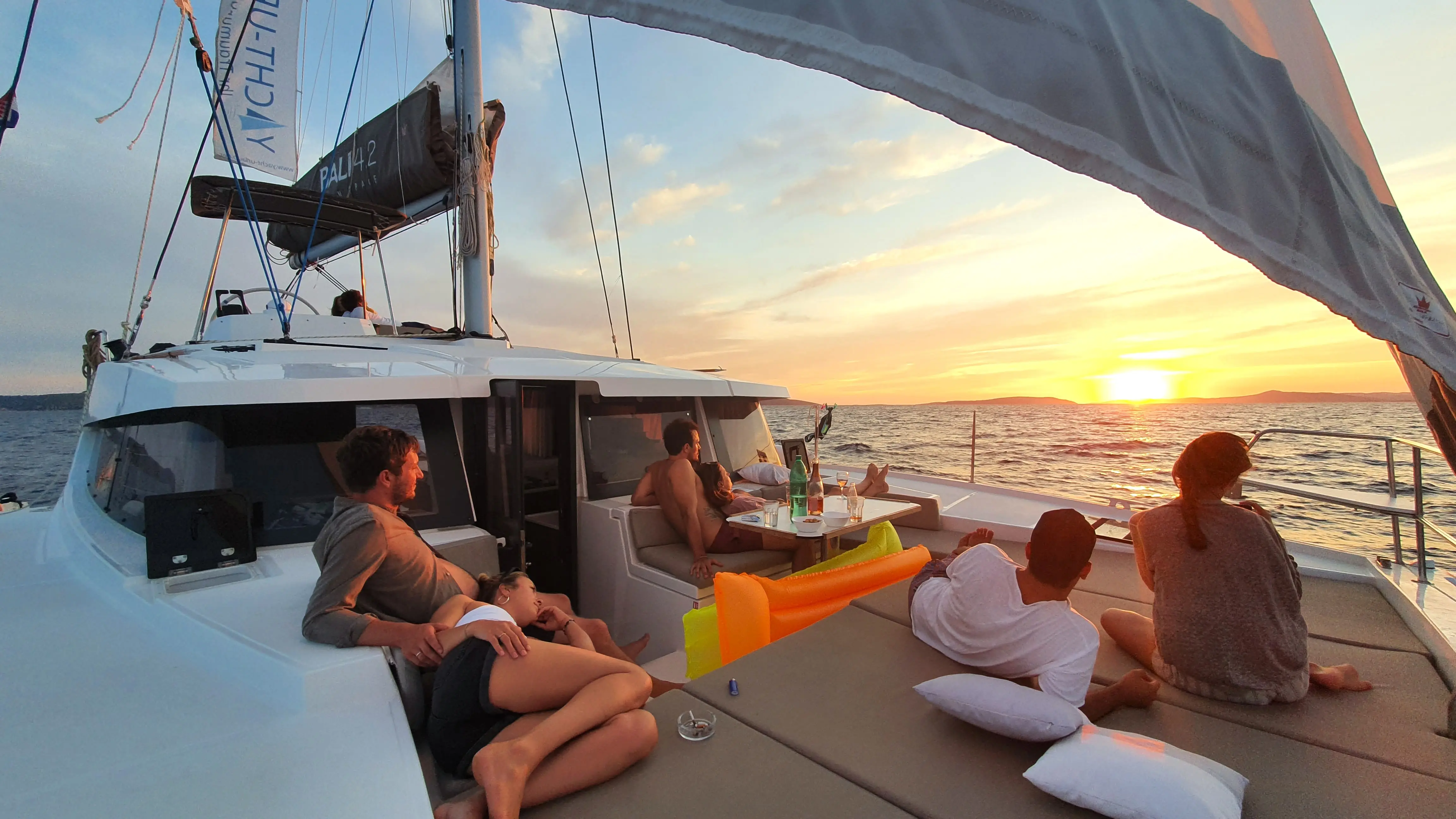 Crew entspannt bei Sonnenuntergang auf dem Vordeck eines Katamarans vor der kroatischen Küste